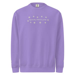 May include: A lavender sweatshirt with the text "repulsively cheerful woman" embroidered in a light yellow color, surrounded by small daisy flower designs. The sweatshirt has a crew neck and long sleeves.
