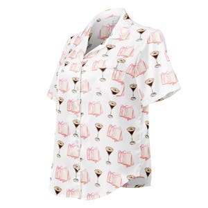 May include: White short-sleeved button-down shirt with a repeating pattern of pink gift boxes and martini glasses. The shirt has a classic collar and a chest pocket. The pattern is in a watercolor style.