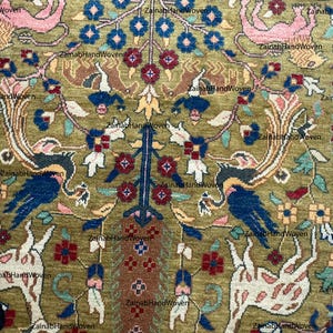 May include: Close-up of a hand-woven rug with an intricate design. The rug features a central tree-like motif with blue, red, and yellow floral elements. The background is olive green, with animal and bird figures.