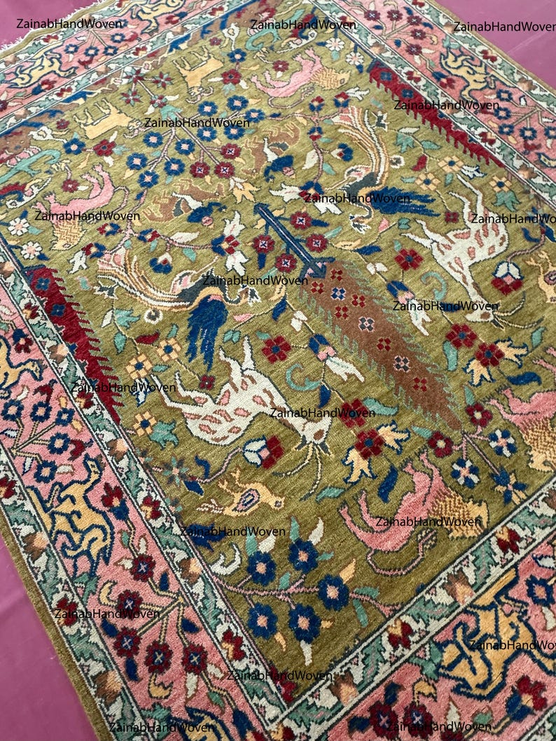 May include: An olive green rug with a detailed pattern featuring floral and animal motifs in shades of pink, blue, and red. The rug has a border with a repeating floral design. The text "ZainabHandWoven" is visible in the image.