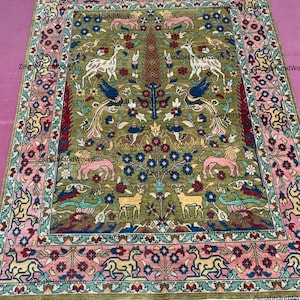 May include: Hand-woven rug with a central olive green field featuring stylized animal and floral motifs in shades of pink, blue, yellow, and brown. The border is a complementary pink with repeating floral patterns. The rug has a fringed edge.