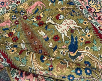 Könnte beinhalten: Handgewebter Teppich in Olivgrün mit detailliertem Blumen- und Tiermuster. Das zentrale Design zeigt Hirsche und Vögel, umgeben von einem Rand aus rosa, blauen und gelben Blumenmotiven. Maße nicht sichtbar.