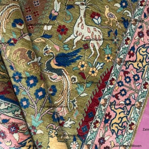 May include: An intricately woven rug with a detailed pattern featuring a deer, birds, and floral elements in shades of green, pink, blue, and red. The rug has a border with a repeating floral design. The text "ZainabHandWoven" is visible.