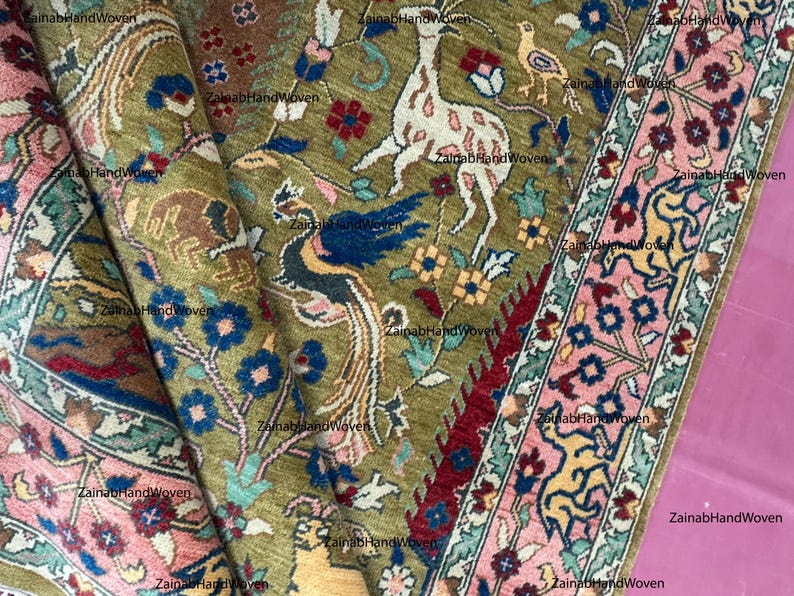 May include: An intricately woven rug with a detailed pattern featuring a deer, birds, and floral elements in shades of green, pink, blue, and red. The rug has a border with a repeating floral design. The text "ZainabHandWoven" is visible.