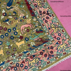 May include: An olive green, hand-woven rug with a detailed pattern. The design features various animals, floral elements, and a border with pink and blue accents. The rug's intricate design and color palette create a visually rich textile.