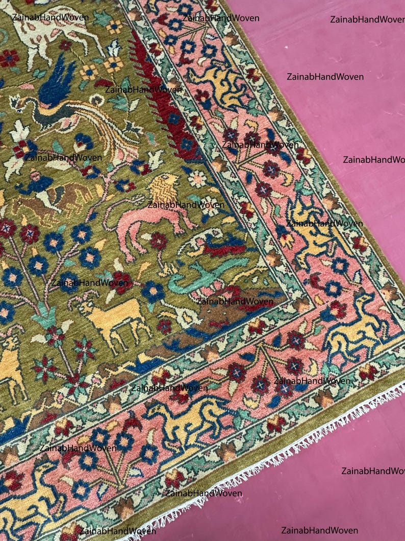 May include: An olive green, hand-woven rug with a detailed pattern. The design features various animals, floral elements, and a border with pink and blue accents. The rug's intricate design and color palette create a visually rich textile.