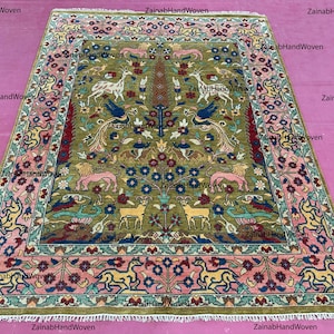 May include: Hand-woven rug with an intricate design featuring deer, birds, and floral motifs in shades of green, pink, blue, and yellow. The rug has a detailed border and a central medallion, showcasing traditional craftsmanship.