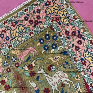 May include: A detailed, hand-woven rug with a central olive green field featuring animal and floral motifs in pink, blue, and white. The border is a contrasting pink with yellow and blue stylized designs. The rug has a fringed edge.