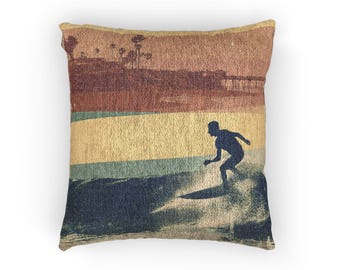 May include: Square throw pillow with a vintage-style illustration of a surfer riding a wave. The design features horizontal stripes in shades of brown, yellow, and blue, with a silhouette of a surfer.