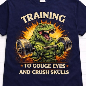 May include: Navy blue t-shirt with a graphic of a green dinosaur lifting a barbell. The text reads "TRAINING" above the dinosaur and "TO GOUGE EYES AND CRUSH SKULLS" below. The design has a retro, cartoon style.