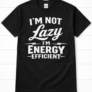 Puede incluir: Camiseta negra con texto blanco: "I'M NOT Lazy I'M ENERGY -EFFICIENT-". El texto es en negrita y sin serifa. La camiseta tiene mangas cortas y cuello redondo.