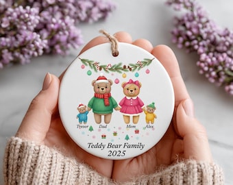 Puede incluir: Adorno navideño redondo de cerámica blanca con una ilustración de una familia de osos de peluche. Los osos visten ropa festiva, con el texto "Teddy Bear Family 2025" en la parte inferior. Se adjunta una cuerda de yute para colgarlo.