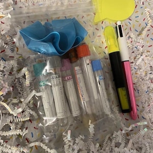 Pu&ograve; includere: Un sacchetto di plastica trasparente contenente diversi flaconi medici con tappi colorati, una fascia elastica blu e una penna multicolore. I flaconi hanno etichette con testo. &Egrave; visibile anche un post-it giallo.