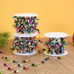 Puede incluir: Tres carretes de luces navideñas de colores con bombillas multicolores. Las luces están en carretes blancos, con algunos hilos de luces que se extienden. Las bombillas son en tonos de rojo, verde, azul y plata.