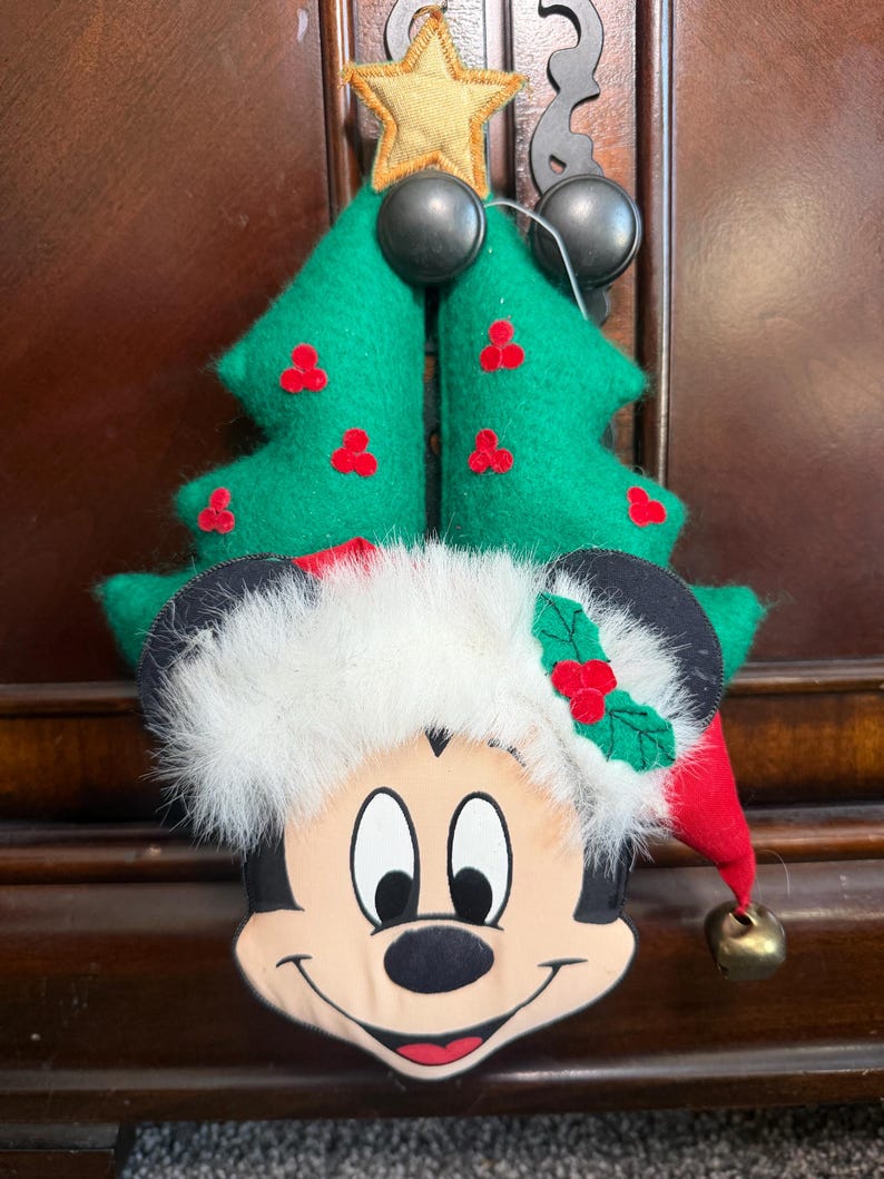 Puede incluir: Adorno navide&ntilde;o para &aacute;rbol con Mickey Mouse. El &aacute;rbol de fieltro verde tiene detalles de bayas rojas y una estrella dorada. Mickey Mouse lleva un gorro de Pap&aacute; Noel con una campana. El adorno est&aacute; dise&ntilde;ado para colgar.