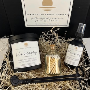 May include: A black gift box containing a black candle jar, a black room and linen spray bottle, a small glass bottle filled with white-tipped matches, and a black metal wick trimmer. All items feature labels with the text Blessing.