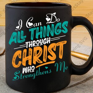 Op de afbeelding: Zwarte keramische mok met een grote handgreep. De mok heeft de tekst "I Can Do All Things Through Christ Who Strengthens Me" in witte, blauwgroene en oranje letters. De mok staat op een neutrale ondergrond.