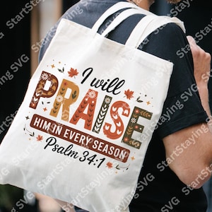 May include: A white canvas tote bag with the text "I will PRAISE HIM IN EVERY SEASON Psalm 34:1" in a decorative, fall-themed design. The text is in various colors, including brown, orange, and red, with floral and leaf accents.
