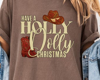 May include: A brown t-shirt with the text "Have a Holly Dolly Christmas" in a vintage style. The design includes a cowboy hat and a pair of cowboy boots. The shirt is a relaxed fit.