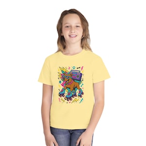 May include: A light yellow t-shirt featuring a cartoon dog wearing sunglasses and roller skates, with a boombox on its back. The graphic has a retro 80s vibe with lightning bolts and paw prints.