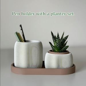 Könnte beinhalten: Ein weißer, gerippter Stifthalter mit Stiften und ein kleiner Pflanztopf mit einer Sukkulente, beides auf einem passenden Tablett. Der Text "Pen holder with a planter set" befindet sich darüber.