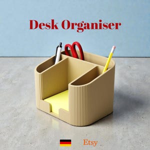 Könnte beinhalten: Ein beiger Schreibtisch-Organizer mit vertikalen Rippendetails. Der Organizer hat mehrere Fächer mit einem Stift, einer Schere und einem Bleistift. Ein gelber Haftnotizblock ist vorne sichtbar. Der Text "Desk Organiser" wird in Rot angezeigt.