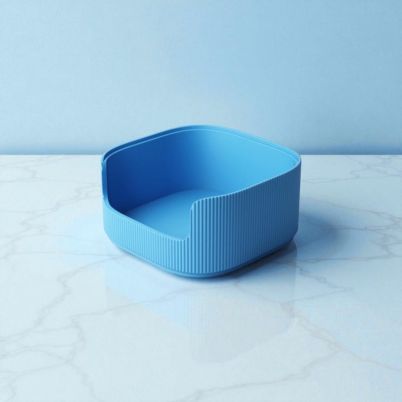 May include: A light blue, square-shaped container with a ribbed exterior and a smooth interior. The container has rounded corners and a low, open side. The background is a solid light blue, and the surface is white with gray veining.