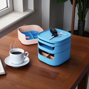 May include: A blue and pink storage organizer with multiple compartments sits on a wooden table. A cup of coffee and a small container are also on the table. Keys rest on top of the organizer.