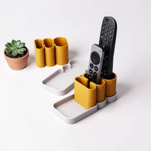 Könnte beinhalten: Ein modernes Schreibtisch-Organizer-Set in Senfgelb und Grau. Das Set beinhaltet einen Fernbedienungshalter, ein Tablett und eine kleine Sukkulente in einem Terrakotta-Topf. Der Fernbedienungshalter hat drei Fächer. Das Tablett ist rechteckig.
