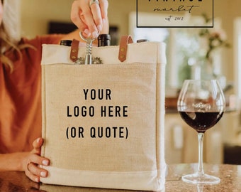 May include: A beige canvas tote bag with brown leather handles and a metal bottle opener. The bag has the text "YOUR LOGO HERE (OR QUOTE)" printed on the front. The bag is sitting on a brown countertop next to a glass of red wine.