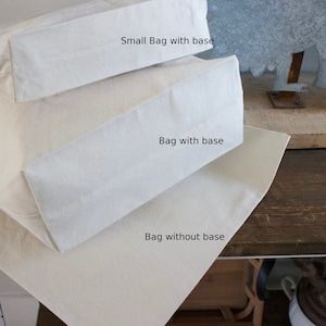 May include: Three white canvas tote bags stacked on top of each other. The top bag is labeled "Small Bag with base", the middle bag is labeled "Bag with base", and the bottom bag is labeled "Bag without base".
