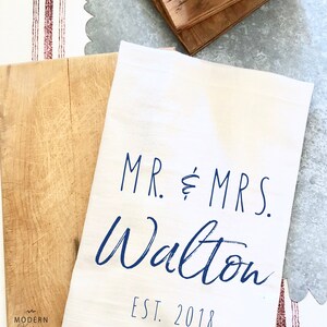 May include: White kitchen towel with blue text that reads "MR. & MRS. Walton EST. 2018".