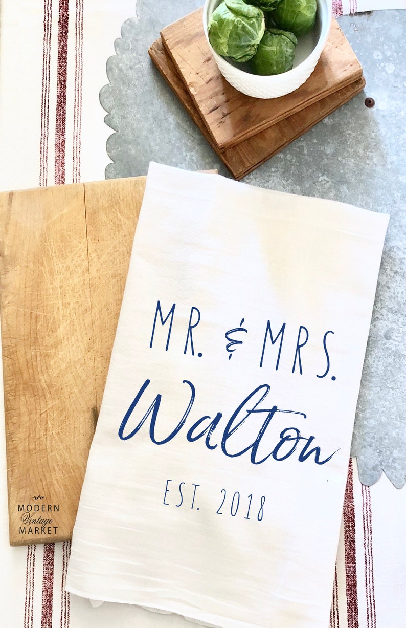 May include: White kitchen towel with blue text that reads "MR. & MRS. Walton EST. 2018".