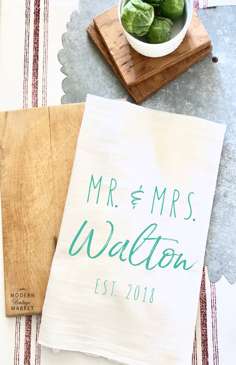 May include: White kitchen towel with the text "MR. & MRS. Walton EST. 2018" in teal green lettering.