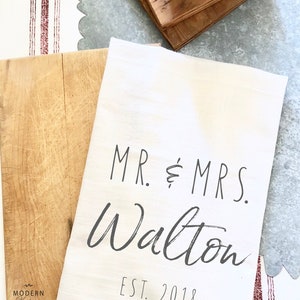 May include: White kitchen towel with black text that reads "MR. & MRS. Walton EST. 2018".