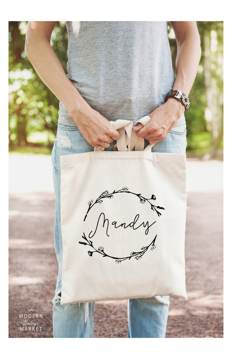 May include: A white canvas tote bag with black floral wreath and the name "Mandy" printed in a cursive font.