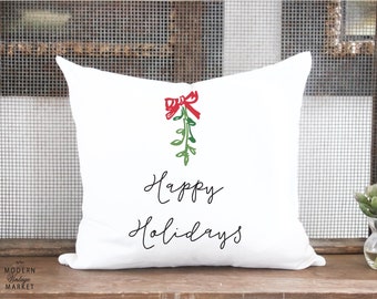 May include: White pillow with a green and red mistletoe design and the text "Happy Holidays" in black cursive writing.