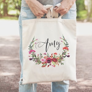 May include: A white canvas tote bag with a floral wreath design and the name "Amy" printed in black script.