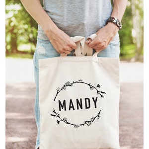 May include: A white canvas tote bag with black floral wreath design and the name "MANDY" printed in the center.