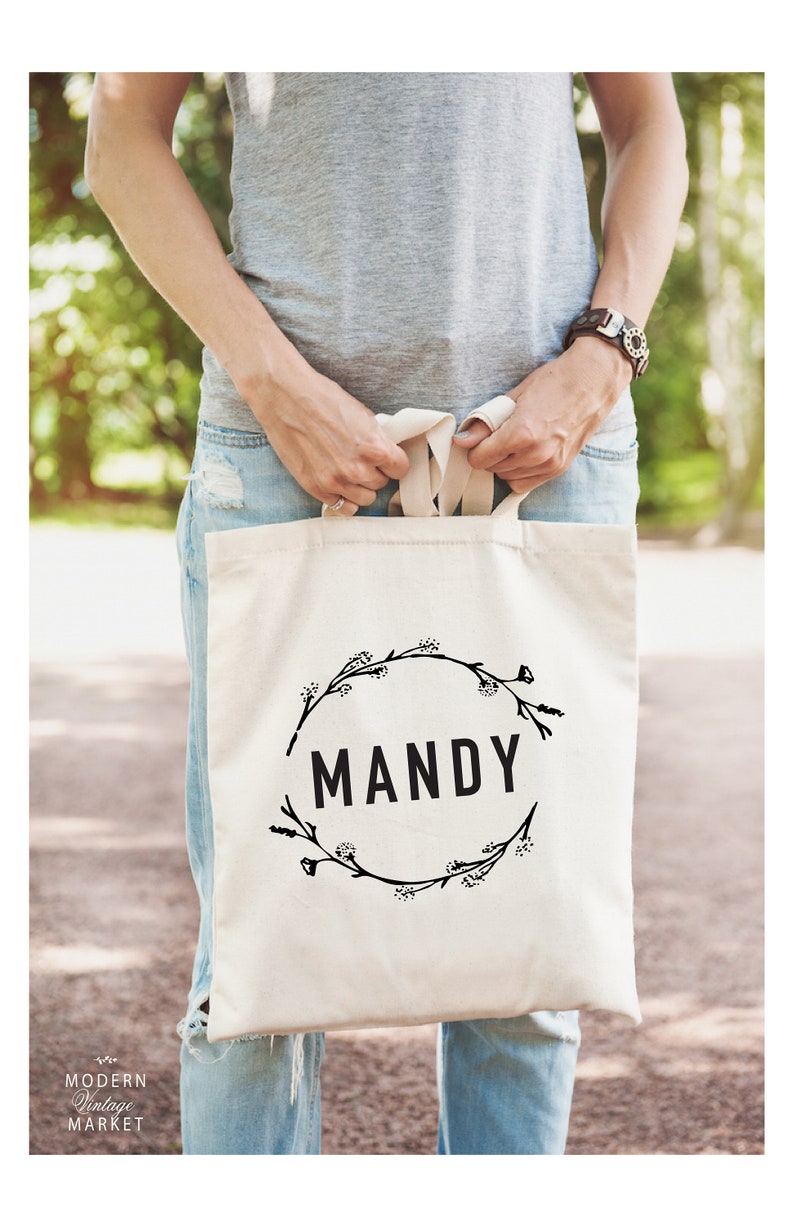 May include: A white canvas tote bag with black floral wreath design and the name "MANDY" printed in the center.