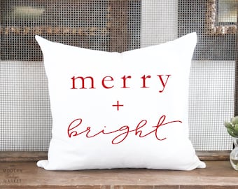 May include: White throw pillow with red text that reads "merry + bright".
