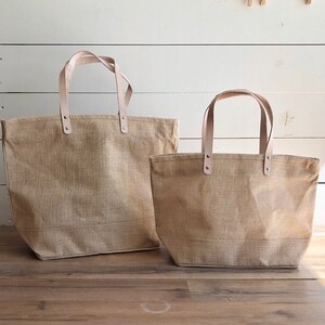 Op de afbeelding: Twee bruine jute tassen met leren handvatten. De grotere tas is op de achtergrond en de kleinere tas is op de voorgrond.
