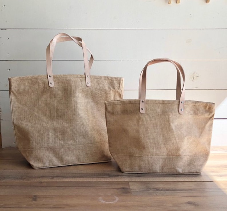 Op de afbeelding: Twee bruine jute tassen met leren handvatten. De grotere tas is op de achtergrond en de kleinere tas is op de voorgrond.