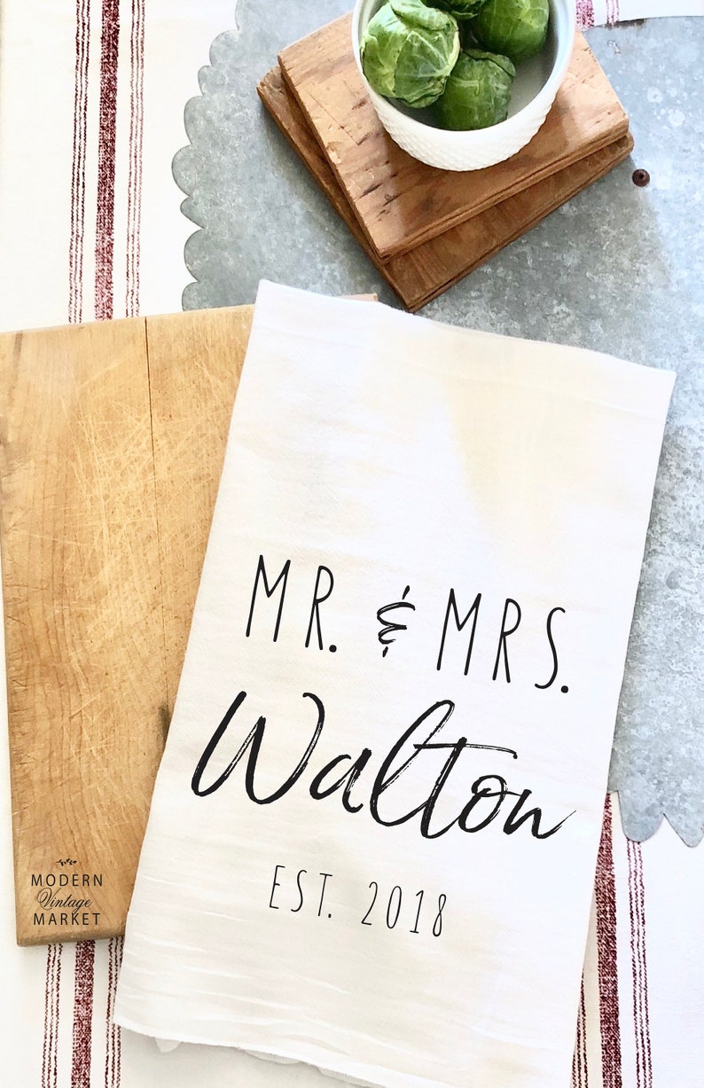 May include: White kitchen towel with black text that reads "MR. & MRS. Walton EST. 2018".