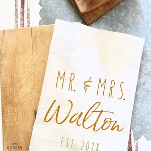 May include: White kitchen towel with the text "MR. & MRS. Walton EST. 2018" in gold lettering.