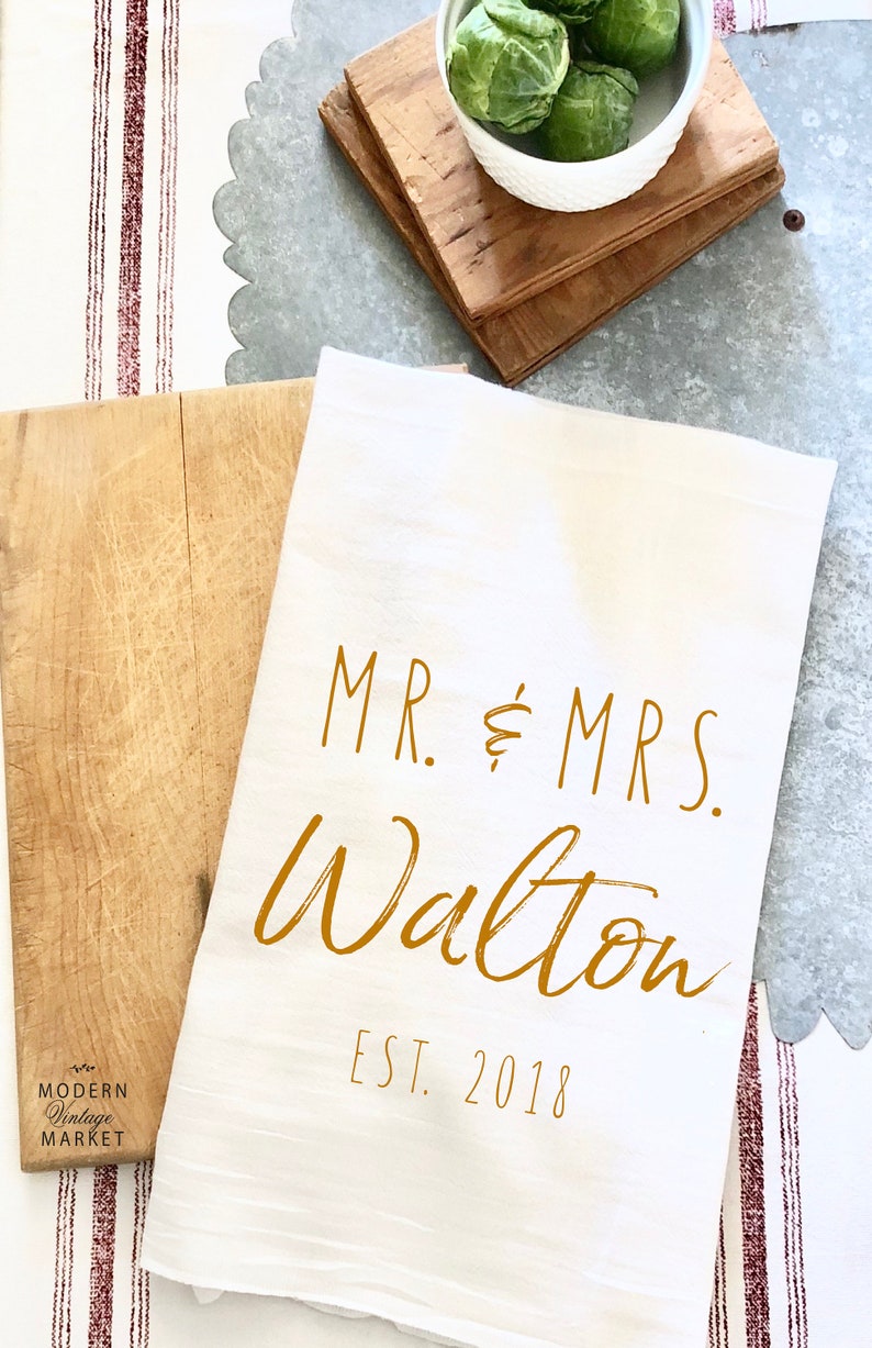 May include: White kitchen towel with the text "MR. & MRS. Walton EST. 2018" in gold lettering.