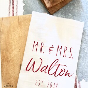 May include: White kitchen towel with the text "MR. & MRS. Walton EST. 2018" in red.