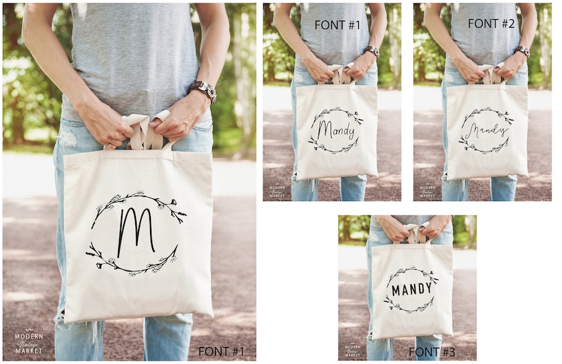 May include: Three tote bags with different fonts and designs. The first bag has a simple 'M' in a wreath. The second bag has the name 'Mandy' in a cursive font in a wreath. The third bag has the name 'MANDY' in a block font in a wreath.