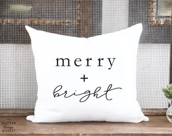 May include: White throw pillow with black text that reads "merry + bright".