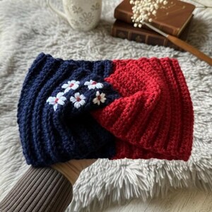May include: A handmade, crocheted headband in a split design. One side is navy blue with white floral embroidery, and the other is red. The headband is made of a thick, textured yarn.
